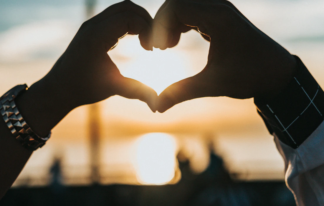 Two people making a heart with their hands at sunset